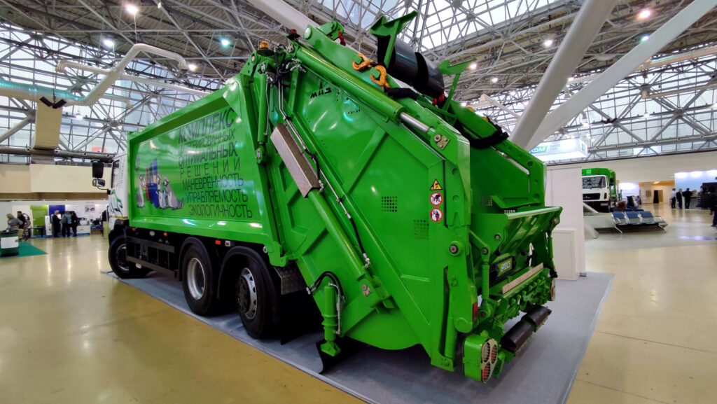 Задний вид мусоровоза МАЗ с зелёной платформой и гидравлической системой