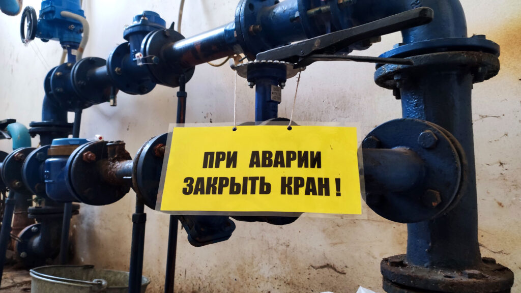 Водопроводные трубы и табличка с указанием закрыть кран при аварии